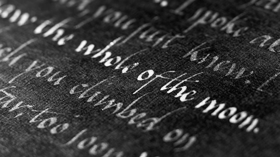 Primer plano macro de caligrafía artística con tinta blanca sobre papel negro texturizado, mostrando el detalle del trazo y la fibra del papel.